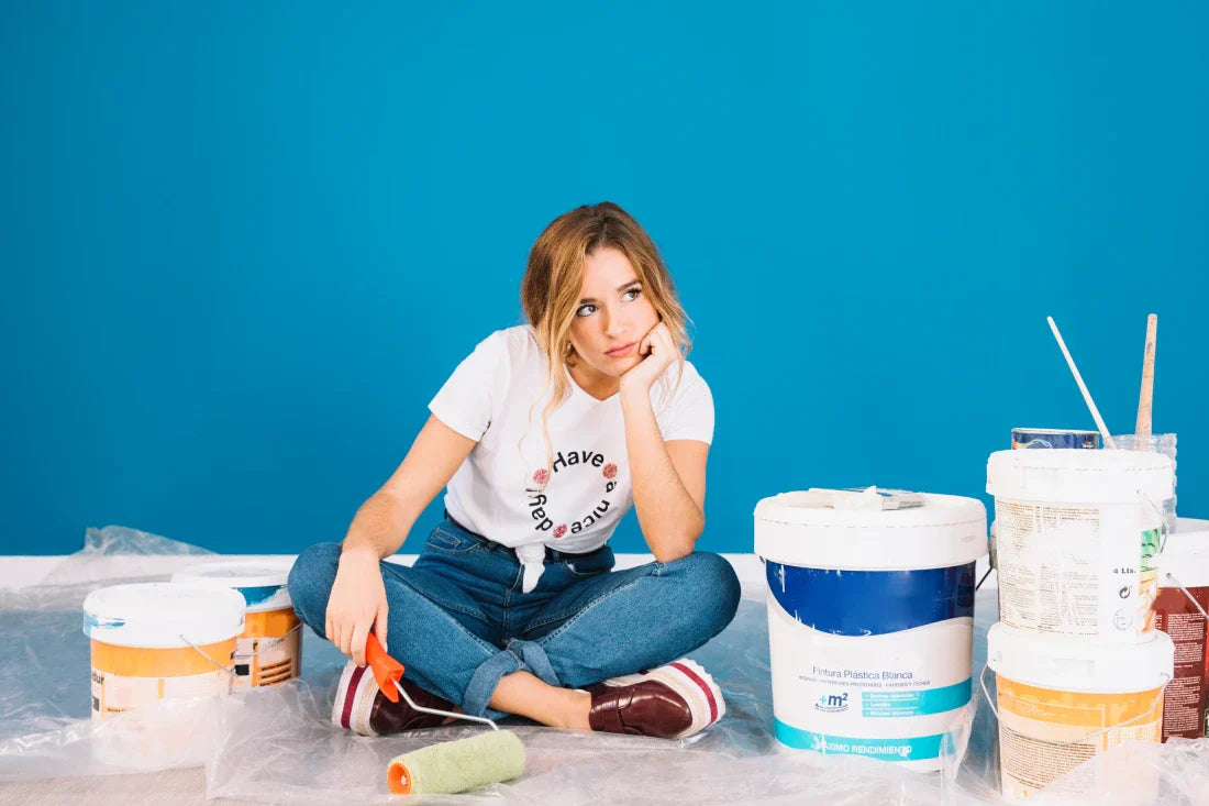 Homeowner sitting with paint roller and paint buckets before interior painting project
